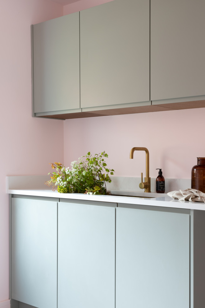 Design ideas for a large contemporary single-wall laundry room in Oxfordshire with a drop-in sink, flat-panel cabinets, green cabinets, quartzite benchtops, multi-coloured splashback, engineered quartz splashback, pink walls, ceramic floors, a side-by-side washer and dryer, grey floor and multi-coloured benchtop.