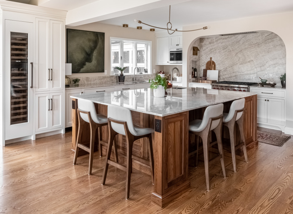 Design ideas for a large transitional l-shaped eat-in kitchen in Philadelphia with an undermount sink, shaker cabinets, white cabinets, quartzite benchtops, beige splashback, stone slab splashback, panelled appliances, medium hardwood floors, with island, brown floor and beige benchtop.
