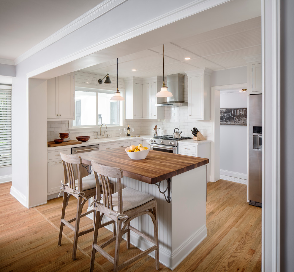Mid-sized elegant u-shaped light wood floor eat-in kitchen photo in Miami with beaded inset cabinets, white cabinets, wood countertops, white backsplash, ceramic backsplash, an island, an undermount sink and stainless steel appliances