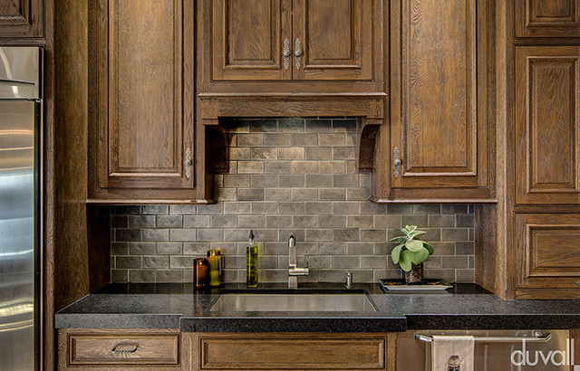 Kitchen - rustic light wood floor kitchen idea with brown cabinets, granite countertops, gray backsplash, brick backsplash, stainless steel appliances and an island
