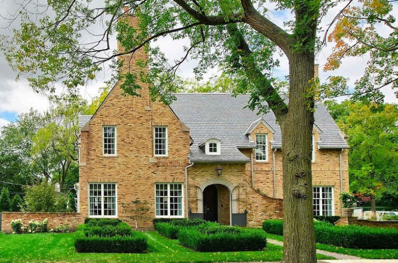 Large traditional two-storey brick yellow house exterior in Chicago with a clipped gable roof and a shingle roof.