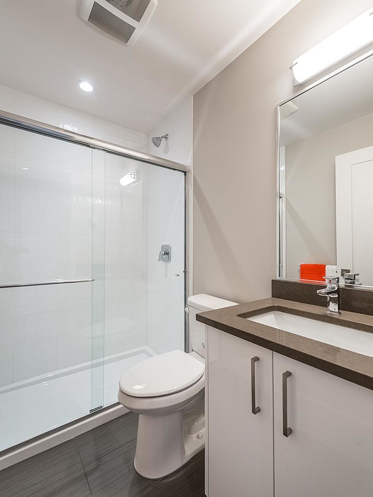 Photo of a mid-sized contemporary 3/4 bathroom in Vancouver with flat-panel cabinets, white cabinets, an alcove shower, a two-piece toilet, white tile, ceramic tile, grey walls, an undermount sink, solid surface benchtops and grey benchtops.