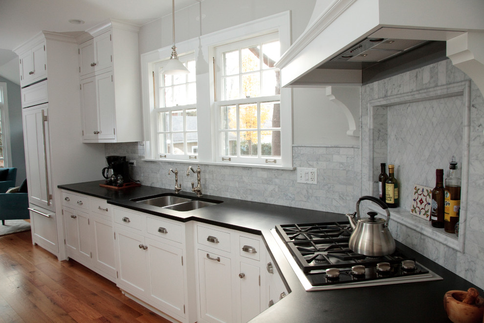 Enclosed kitchen - mid-sized transitional u-shaped medium tone wood floor enclosed kitchen idea in Chicago with a double-bowl sink, beaded inset cabinets, white cabinets, soapstone countertops, gray backsplash, stone tile backsplash, paneled appliances and a peninsula