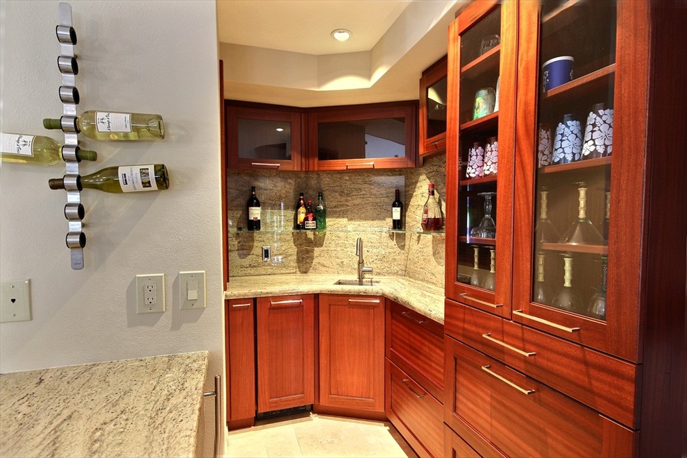 This is an example of a small tropical l-shaped home bar in Hawaii with recessed-panel cabinets, medium wood cabinets, granite benchtops and travertine floors.