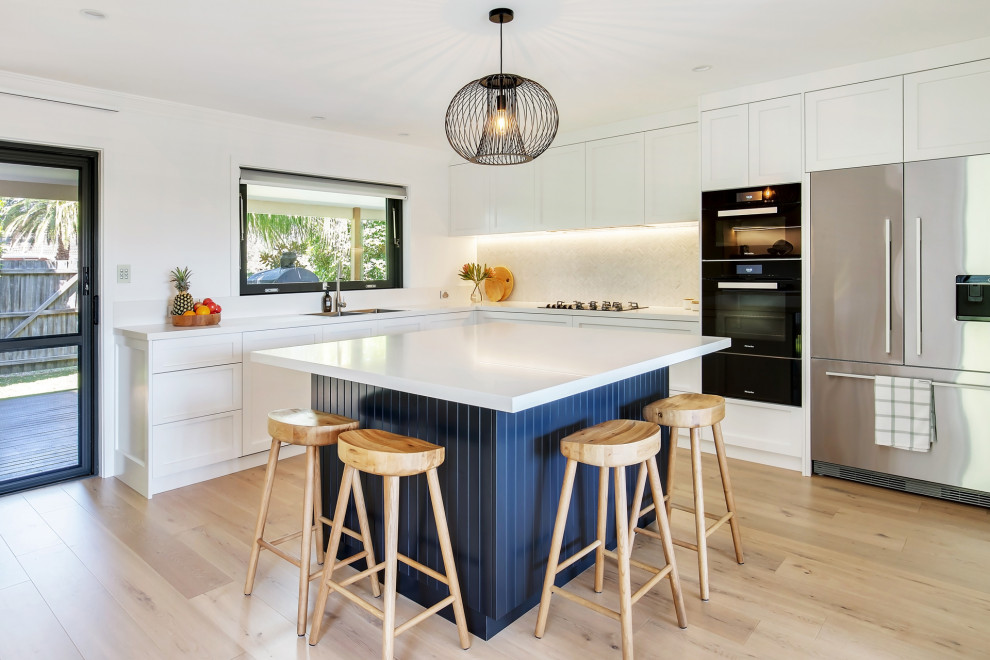 Design ideas for a large beach style l-shaped kitchen pantry in Sydney with a double-bowl sink, shaker cabinets, blue cabinets, quartz benchtops, white splashback, mosaic tile splashback, stainless steel appliances, light hardwood floors, with island, multi-coloured floor, white benchtop and recessed.