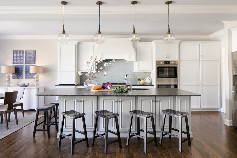 This is an example of a transitional kitchen in Kansas City with an undermount sink, shaker cabinets, white cabinets, grey splashback, subway tile splashback, stainless steel appliances, dark hardwood floors, with island and brown floor.