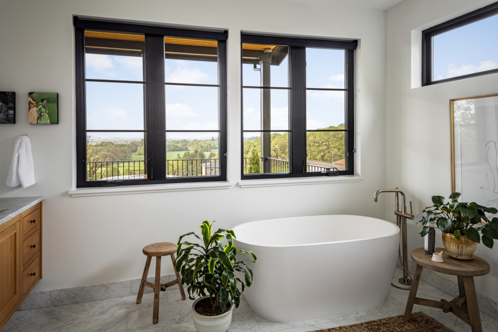 На фото: главная ванная комната среднего размера в современном стиле с фасадами в стиле шейкер, фасадами цвета дерева среднего тона, отдельно стоящей ванной, белыми стенами, мраморным полом и подвесной тумбой с