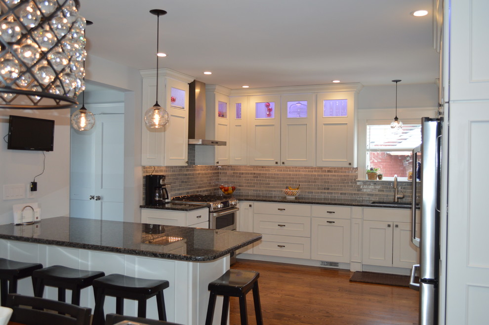 Mid-sized transitional l-shaped medium tone wood floor eat-in kitchen photo in Boston with an undermount sink, recessed-panel cabinets, white cabinets, granite countertops, gray backsplash, cement tile backsplash, stainless steel appliances, a peninsula and blue countertops