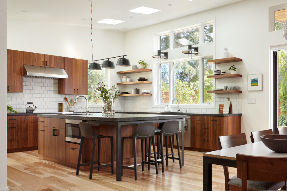 This is an example of a contemporary l-shaped kitchen in San Francisco with flat-panel cabinets, medium wood cabinets, white splashback, stainless steel appliances, with island and grey benchtop.
