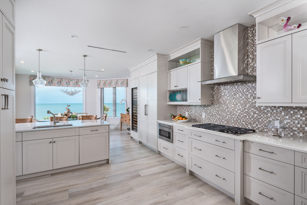 Large beach style l-shaped eat-in kitchen in Miami with an undermount sink, recessed-panel cabinets, quartzite benchtops, multi-coloured splashback, glass tile splashback, panelled appliances, porcelain floors, with island, beige floor, white benchtop and grey cabinets.