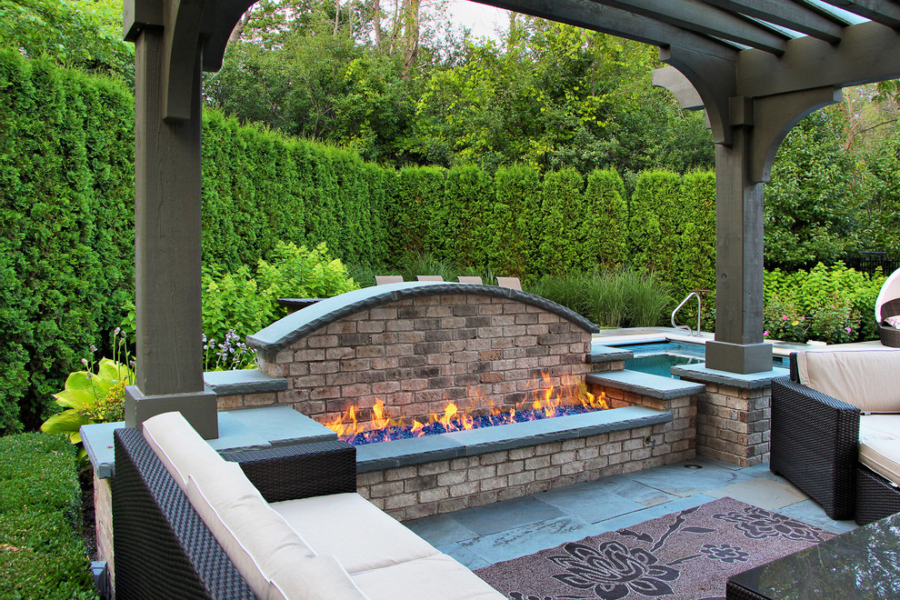 This is an example of a traditional backyard patio in Chicago with a fire feature, natural stone pavers and a pergola.