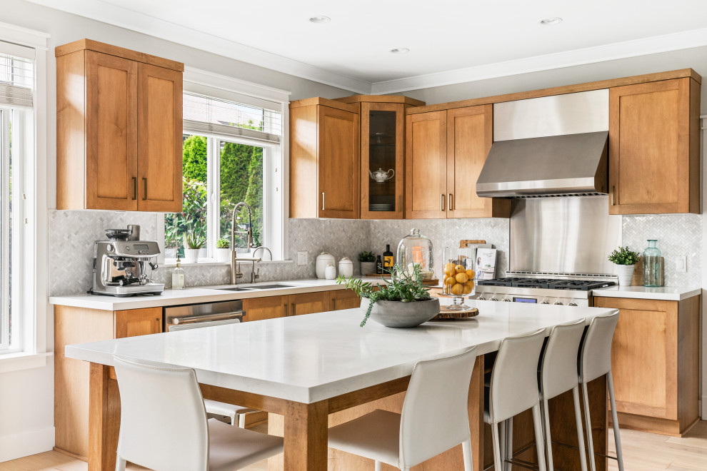 This is an example of a transitional l-shaped kitchen in Vancouver with an undermount sink, shaker cabinets, medium wood cabinets, grey splashback, mosaic tile splashback, stainless steel appliances, light hardwood floors, with island, beige floor and white benchtop.