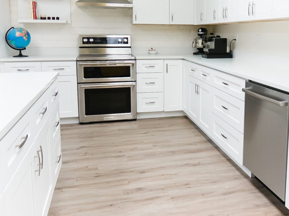 Bild på ett mellanstort funkis vit vitt kök, med en undermonterad diskho, skåp i shakerstil, vita skåp, laminatbänkskiva, vitt stänkskydd, stänkskydd i sten, rostfria vitvaror, vinylgolv, en köksö och brunt golv