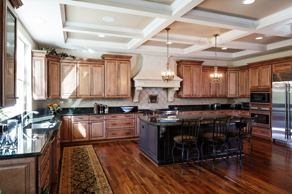 Expansive traditional u-shaped separate kitchen in DC Metro with an undermount sink, raised-panel cabinets, medium wood cabinets, marble benchtops, beige splashback, limestone splashback, stainless steel appliances, medium hardwood floors, with island, brown floor and green benchtop.
