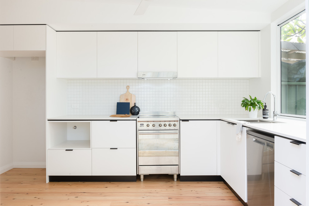 Photo of a small contemporary l-shaped eat-in kitchen in Sydney with an undermount sink, flat-panel cabinets, white cabinets, quartz benchtops, white splashback, mosaic tile splashback, stainless steel appliances, medium hardwood floors, no island and white benchtop.