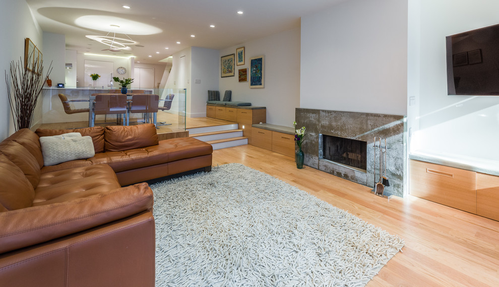 Inspiration for an expansive contemporary open concept family room in New York with white walls, light hardwood floors, a standard fireplace, a concrete fireplace surround, a wall-mounted tv and brown floor.