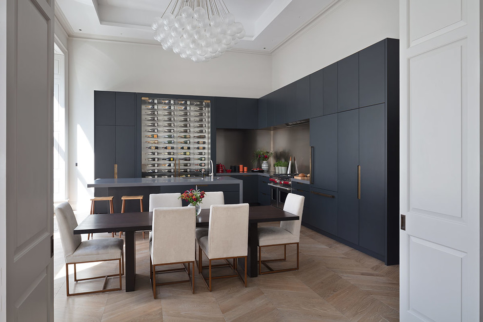 This is an example of an expansive contemporary galley open plan kitchen in London with an undermount sink, glass-front cabinets, grey cabinets, solid surface benchtops, light hardwood floors, with island, brown floor and grey benchtop.