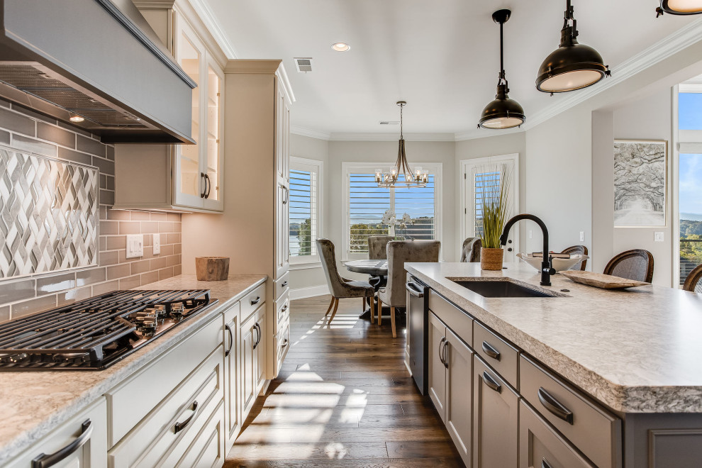 Large transitional l-shaped open concept kitchen photo with an undermount sink, raised-panel cabinets, white cabinets, quartz countertops, gray backsplash, subway tile backsplash, stainless steel appliances, an island and white countertops