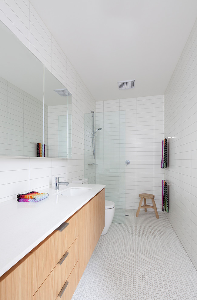 Photo of a midcentury 3/4 bathroom in Melbourne with flat-panel cabinets, light wood cabinets, a curbless shower, white tile, white walls, mosaic tile floors, an undermount sink, white floor, an open shower and white benchtops.