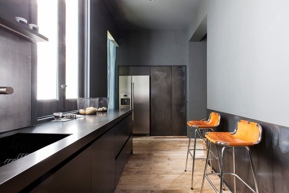 Photo of a mid-sized contemporary single-wall separate kitchen in Madrid with an integrated sink, flat-panel cabinets, grey cabinets, concrete benchtops, black splashback, stainless steel appliances, light hardwood floors and no island.