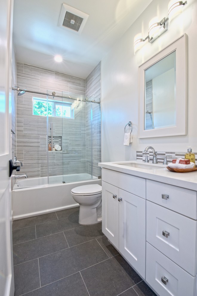 Photo of a mid-sized transitional 3/4 bathroom in Los Angeles with shaker cabinets, white cabinets, a drop-in tub, a shower/bathtub combo, gray tile, ceramic tile, white walls, a drop-in sink, grey floor, a sliding shower screen and white benchtops.