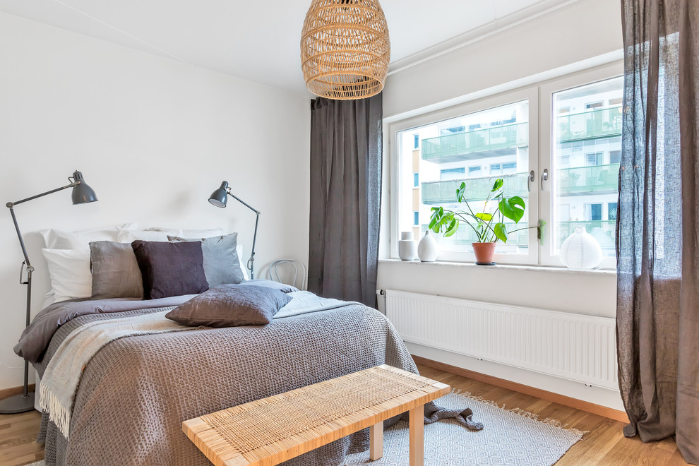 Scandinavian guest bedroom in Stockholm with white walls, medium hardwood floors and beige floor.