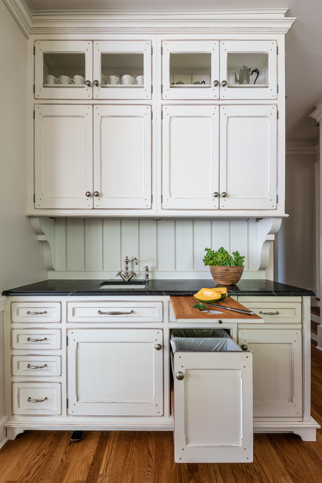 Design ideas for a large transitional u-shaped separate kitchen in DC Metro with a farmhouse sink, recessed-panel cabinets, white cabinets, soapstone benchtops, white splashback, panelled appliances, medium hardwood floors, with island, brown floor and black benchtop.