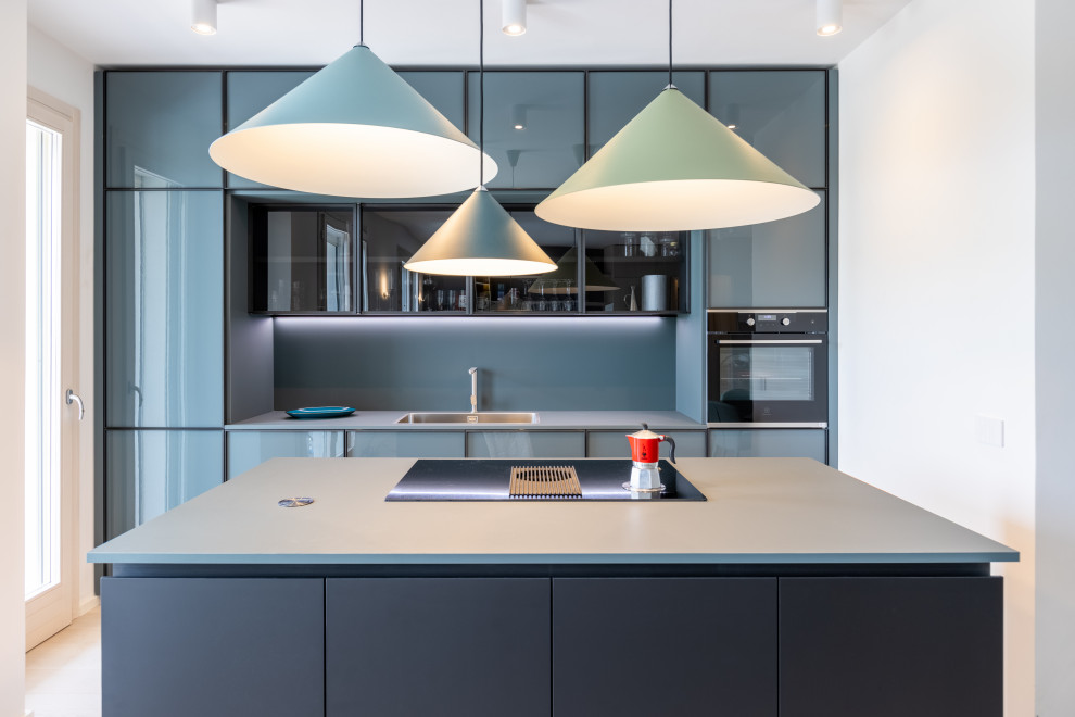 Inspiration for a mid-sized contemporary galley open plan kitchen in Rome with an undermount sink, glass-front cabinets, turquoise cabinets, solid surface benchtops, black splashback, light hardwood floors, with island, beige floor and black benchtop.