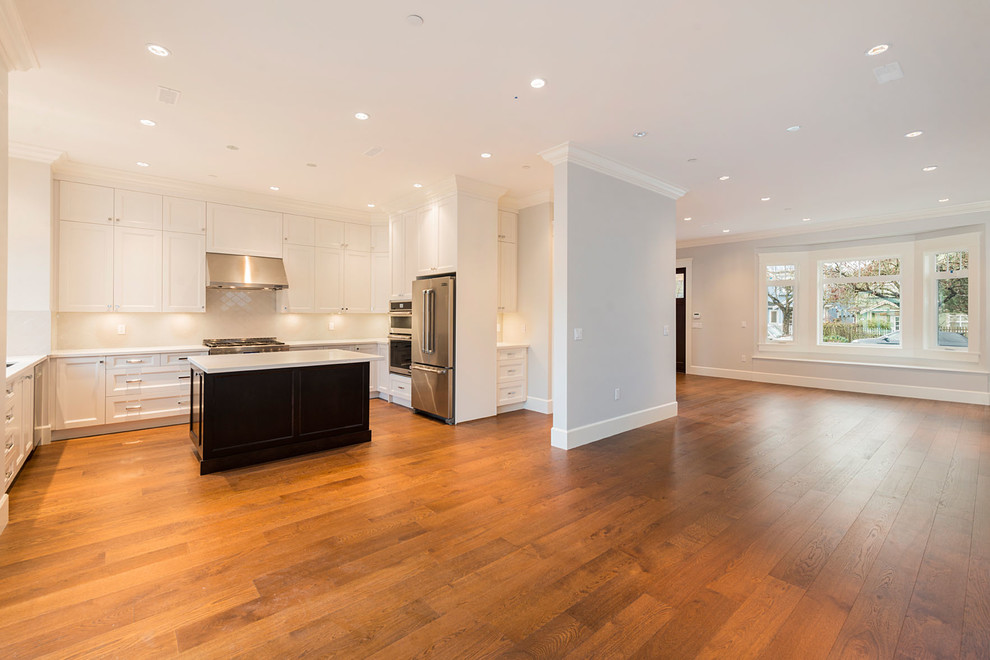 Large transitional u-shaped eat-in kitchen in Vancouver with an undermount sink, white cabinets, solid surface benchtops, white splashback, ceramic splashback, stainless steel appliances, dark hardwood floors, with island and recessed-panel cabinets.