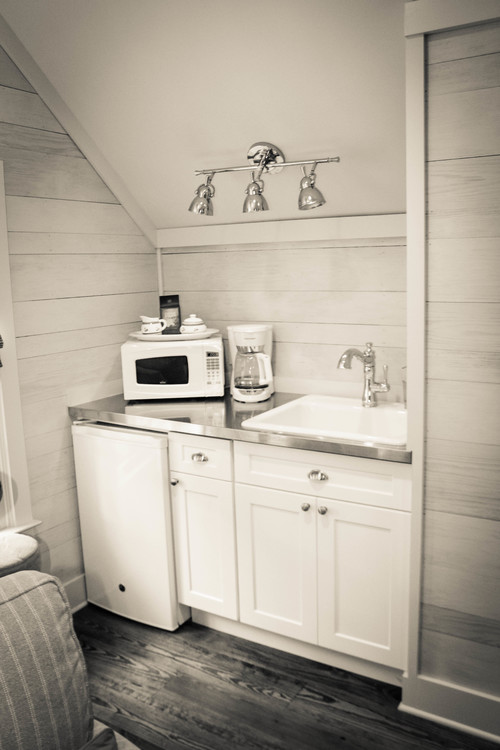 Tiny kitchenette under a sloped ceiling with white shaker kitchen cabinet base, mini fridge, microwave on the counter, and no upper storage