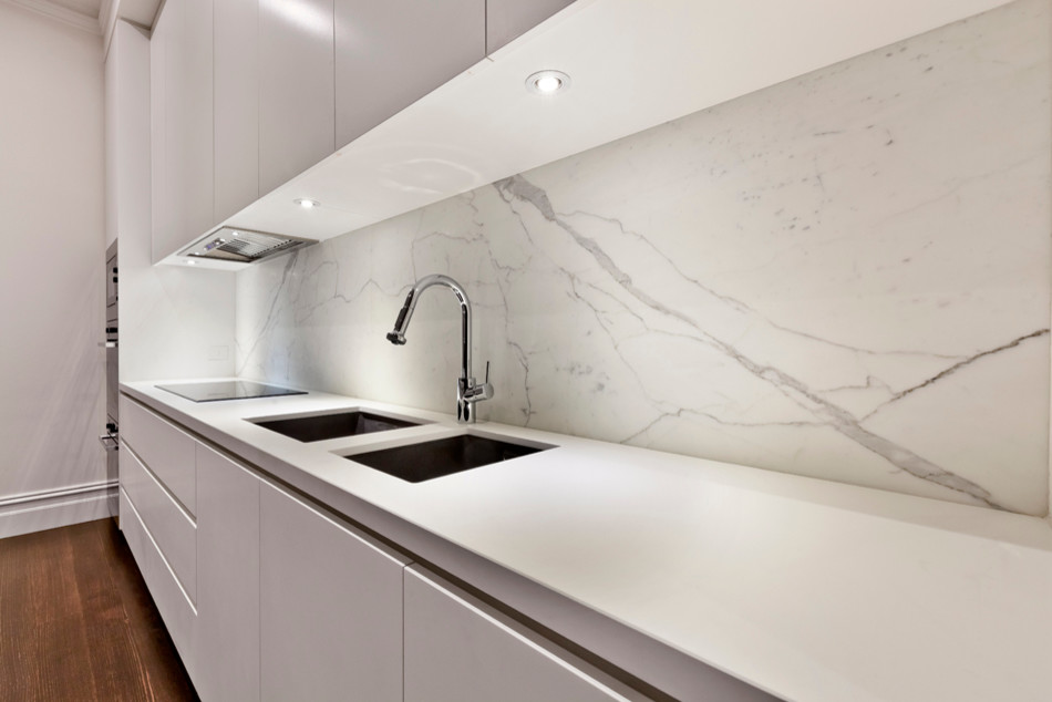 This is an example of a contemporary single-wall eat-in kitchen in Melbourne with an undermount sink, flat-panel cabinets, white cabinets, marble benchtops, white splashback, stone slab splashback, stainless steel appliances, dark hardwood floors and with island.