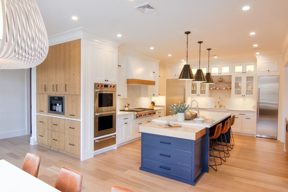 This is an example of a large transitional u-shaped eat-in kitchen in New York with a farmhouse sink, flat-panel cabinets, white cabinets, quartzite benchtops, white splashback, stone slab splashback, stainless steel appliances, light hardwood floors, multiple islands, yellow floor and white benchtop.