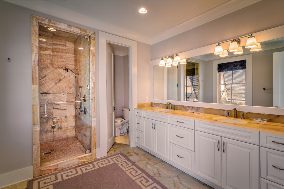 This is an example of a large transitional master bathroom in Charleston with recessed-panel cabinets, white cabinets, an alcove shower, a one-piece toilet, grey walls, marble floors, an undermount sink, glass benchtops, beige floor and a hinged shower door.