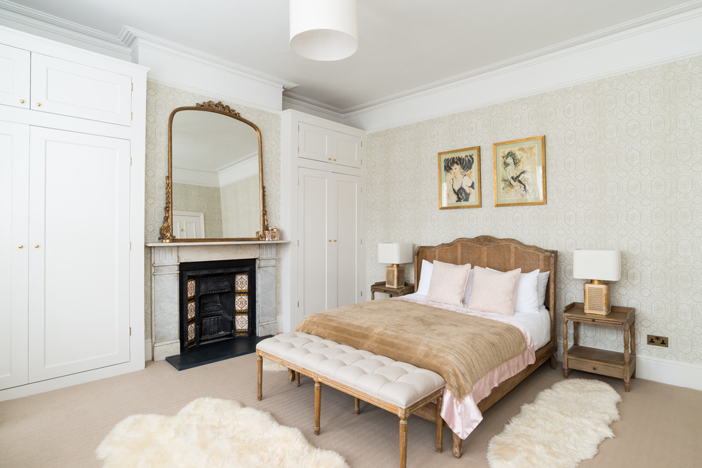 This is an example of a large traditional master bedroom in London with beige walls, carpet, a standard fireplace and beige floor.