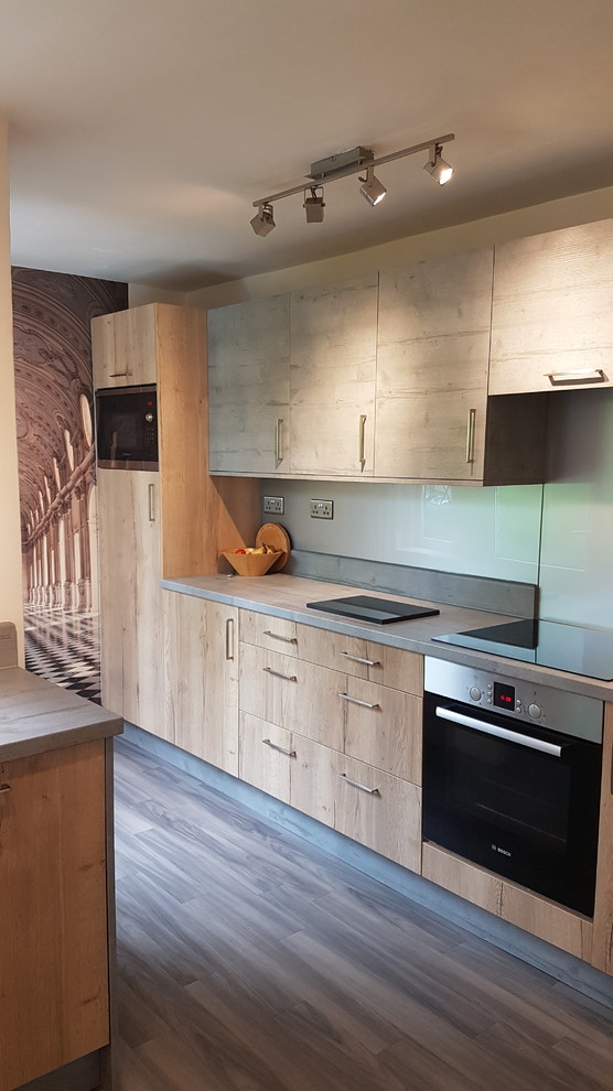 Inspiration for a small traditional single-wall separate kitchen in West Midlands with a drop-in sink, flat-panel cabinets, light wood cabinets, laminate benchtops, grey splashback, glass sheet splashback, stainless steel appliances, laminate floors, no island, grey floor and brown benchtop.