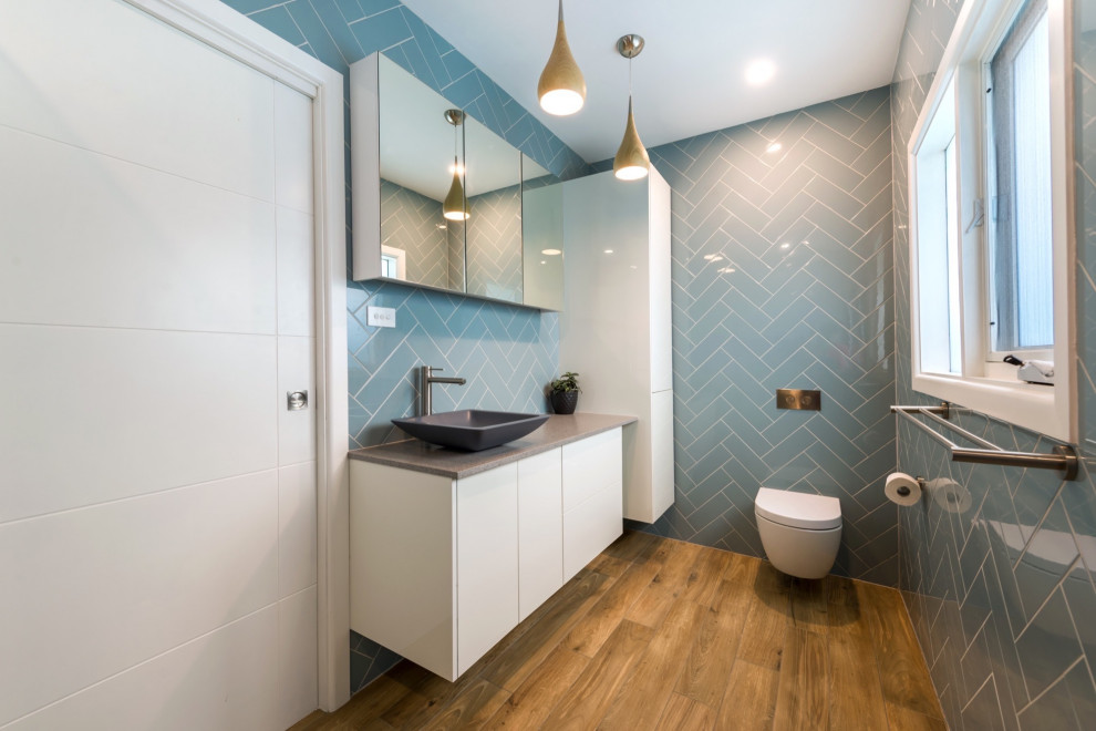 This is an example of a small modern 3/4 bathroom in Other with yellow cabinets, a wall-mount toilet, blue tile, ceramic tile, blue walls, vinyl floors, a vessel sink, granite benchtops, multi-coloured floor, grey benchtops, a single vanity, a floating vanity and decorative wall panelling.