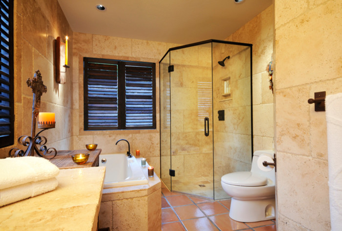 Design ideas for a large mediterranean master bathroom in Other with a two-piece toilet, beige tile, beige walls, terra-cotta floors, wood benchtops, brown floor, a hinged shower door, a corner shower, stone tile and a vessel sink.