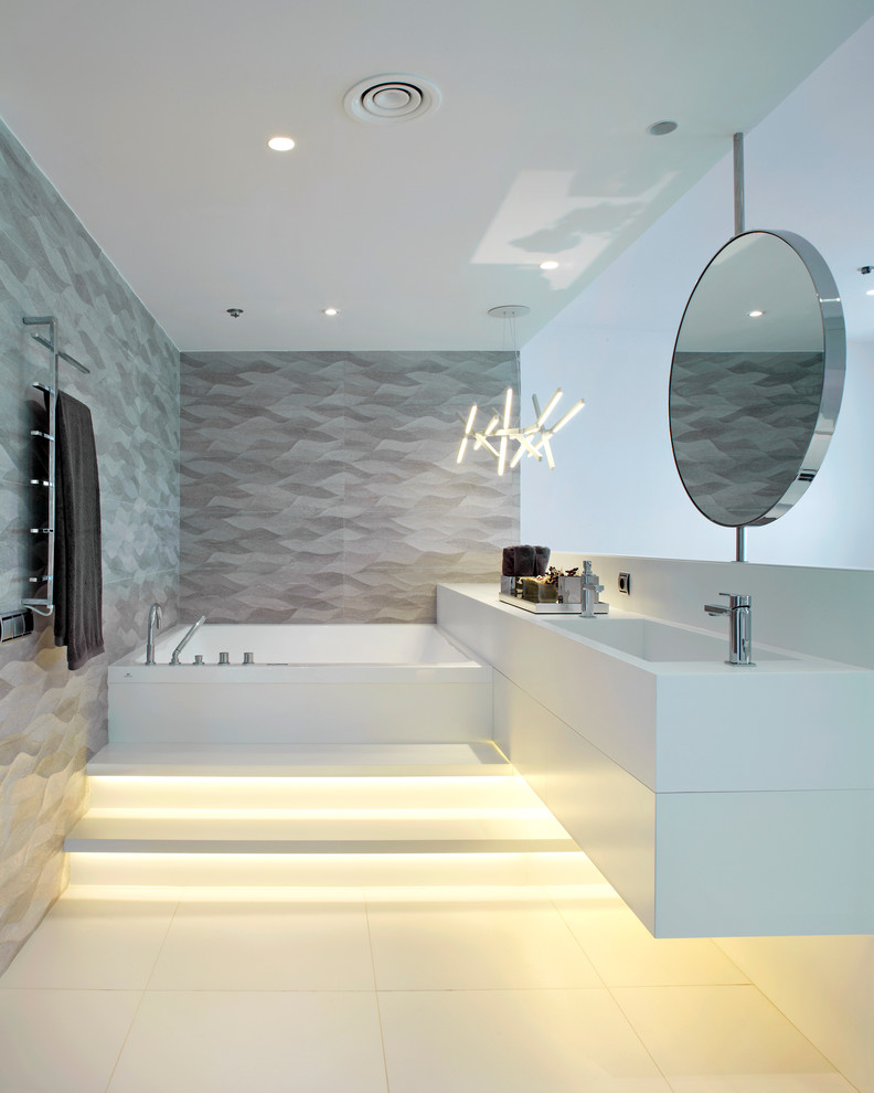 Large contemporary master bathroom in Barcelona with an integrated sink, gray tile, grey walls, ceramic floors, solid surface benchtops and a hot tub.