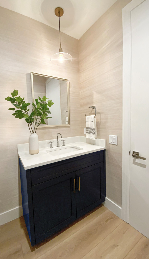Cette image montre un petit WC et toilettes marin avec un placard à porte shaker, des portes de placard bleues, un mur beige, un sol en vinyl, un lavabo encastré, un plan de toilette en quartz modifié, un sol beige, un plan de toilette blanc, meuble-lavabo encastré et du papier peint.