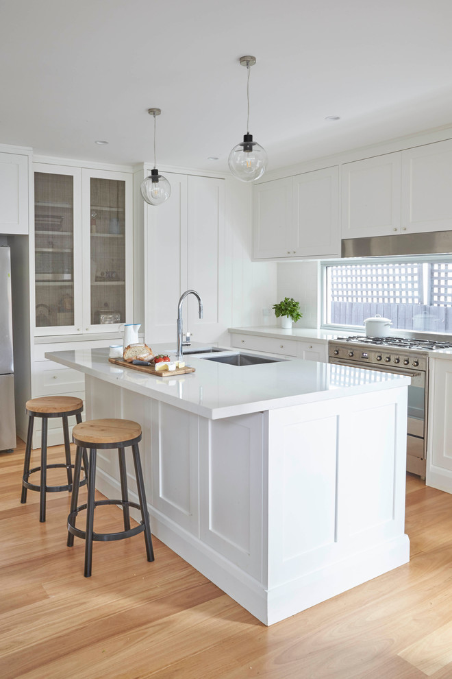 Photo of a mid-sized transitional l-shaped separate kitchen in Sydney with an undermount sink, shaker cabinets, white cabinets, white splashback, ceramic splashback, stainless steel appliances, medium hardwood floors and with island.