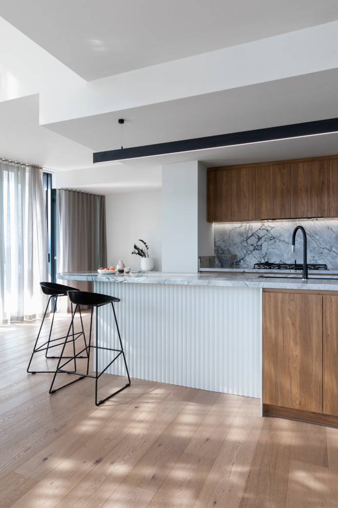 Photo of a medium sized contemporary galley open plan kitchen in Melbourne with a submerged sink, flat-panel cabinets, medium wood cabinets, marble worktops, grey splashback, marble splashback, black appliances, medium hardwood flooring, an island, brown floors and grey worktops.