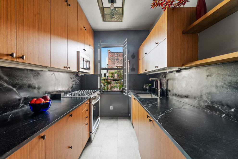 Small arts and crafts galley separate kitchen in New York with an undermount sink, flat-panel cabinets, medium wood cabinets, soapstone benchtops, black splashback, stone slab splashback, stainless steel appliances, grey floor, porcelain floors and black benchtop.