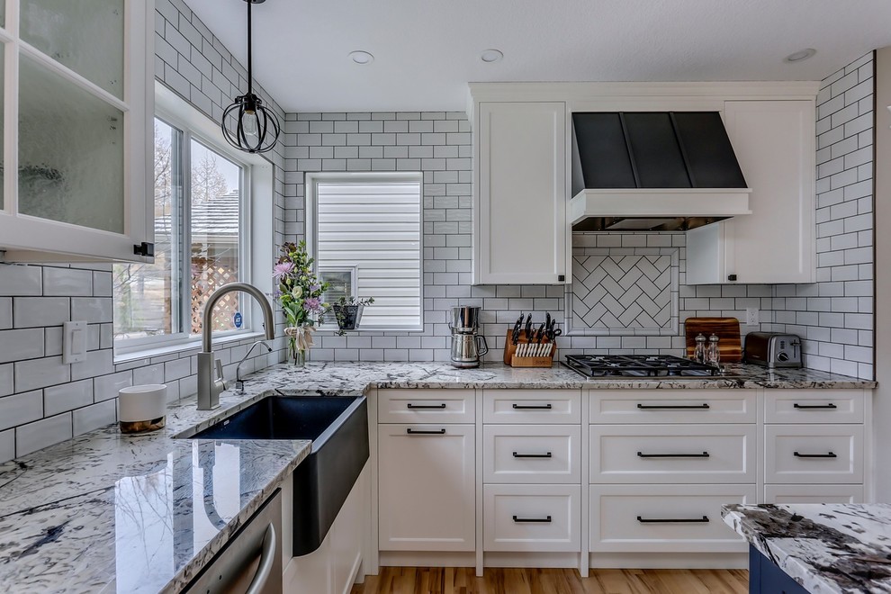 Mid-sized transitional l-shaped eat-in kitchen in Calgary with a farmhouse sink, shaker cabinets, white cabinets, granite benchtops, white splashback, subway tile splashback, stainless steel appliances, light hardwood floors, with island and brown floor.