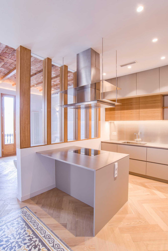Bild på ett mellanstort eklektiskt grå grått kök, med en undermonterad diskho, luckor med infälld panel, grå skåp, bänkskiva i rostfritt stål, grått stänkskydd, stänkskydd i metallkakel, integrerade vitvaror, mellanmörkt trägolv, en köksö och beiget golv