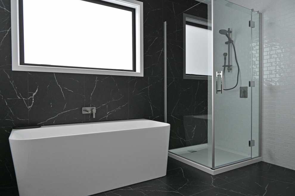 Bild på ett mellanstort svart svart badrum, med luckor med glaspanel, svarta skåp, ett fristående badkar, en hörndusch, svart och vit kakel, marmorkakel, vita väggar, marmorgolv, bänkskiva i akrylsten, svart golv och dusch med gångjärnsdörr