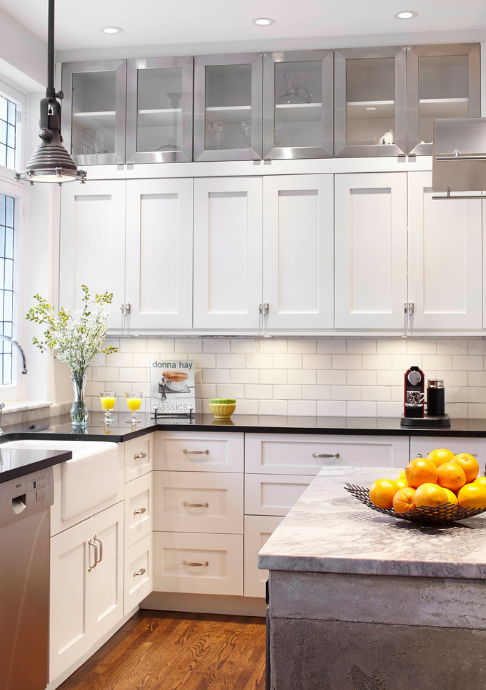 Inspiration for a mid-sized industrial l-shaped eat-in kitchen in Montreal with a farmhouse sink, shaker cabinets, white cabinets, granite benchtops, white splashback, subway tile splashback, stainless steel appliances, medium hardwood floors and with island.