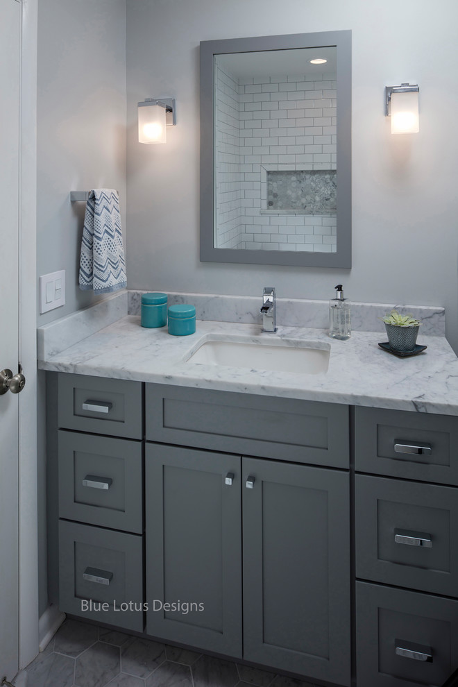 This is an example of a mid-sized traditional kids bathroom in Philadelphia with shaker cabinets, grey cabinets, an alcove tub, an alcove shower, a one-piece toilet, white tile, porcelain tile, grey walls, marble floors, an undermount sink, marble benchtops, multi-coloured floor and a hinged shower door.