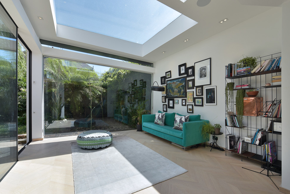 Photo of a contemporary sunroom in London with light hardwood floors, a skylight and beige floor.
