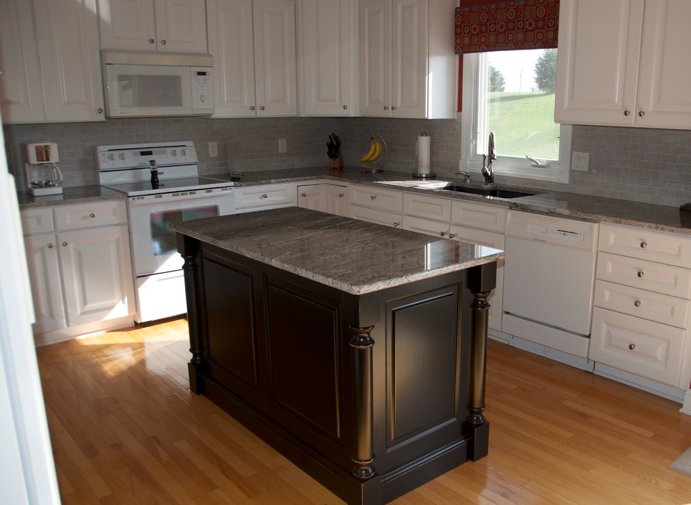 Example of a mid-sized transitional u-shaped medium tone wood floor kitchen design with an undermount sink, flat-panel cabinets, white cabinets, granite countertops, gray backsplash, subway tile backsplash, white appliances and an island