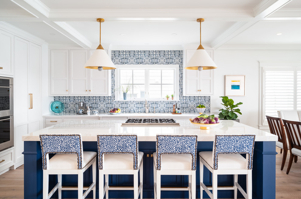 Photo of a mid-sized beach style l-shaped eat-in kitchen in Philadelphia with shaker cabinets, blue splashback, stainless steel appliances, light hardwood floors, with island, brown floor, white benchtop, a farmhouse sink, white cabinets, quartzite benchtops and ceramic splashback.